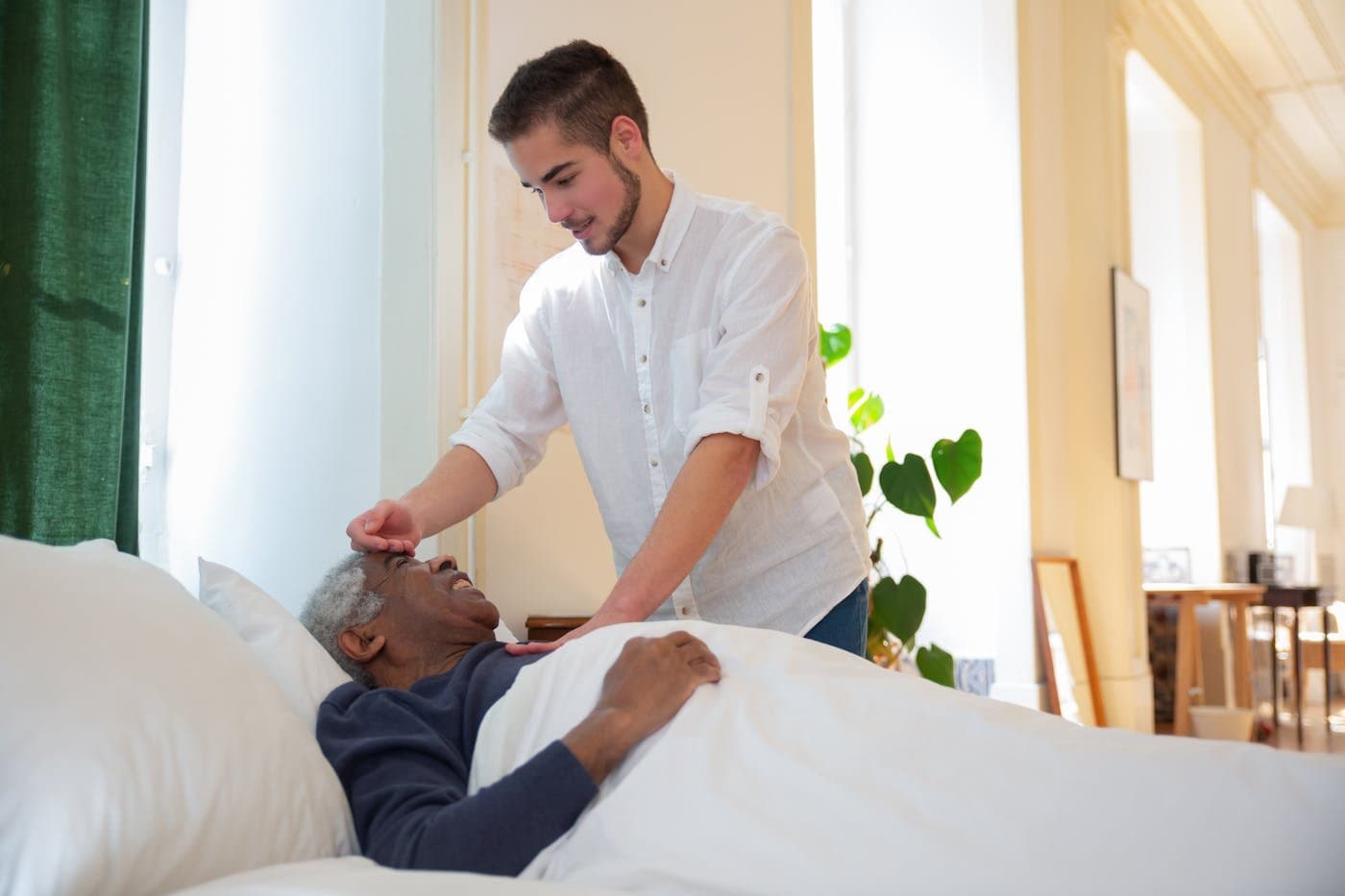 Adult child gently caring for an elderly parent resting in bed