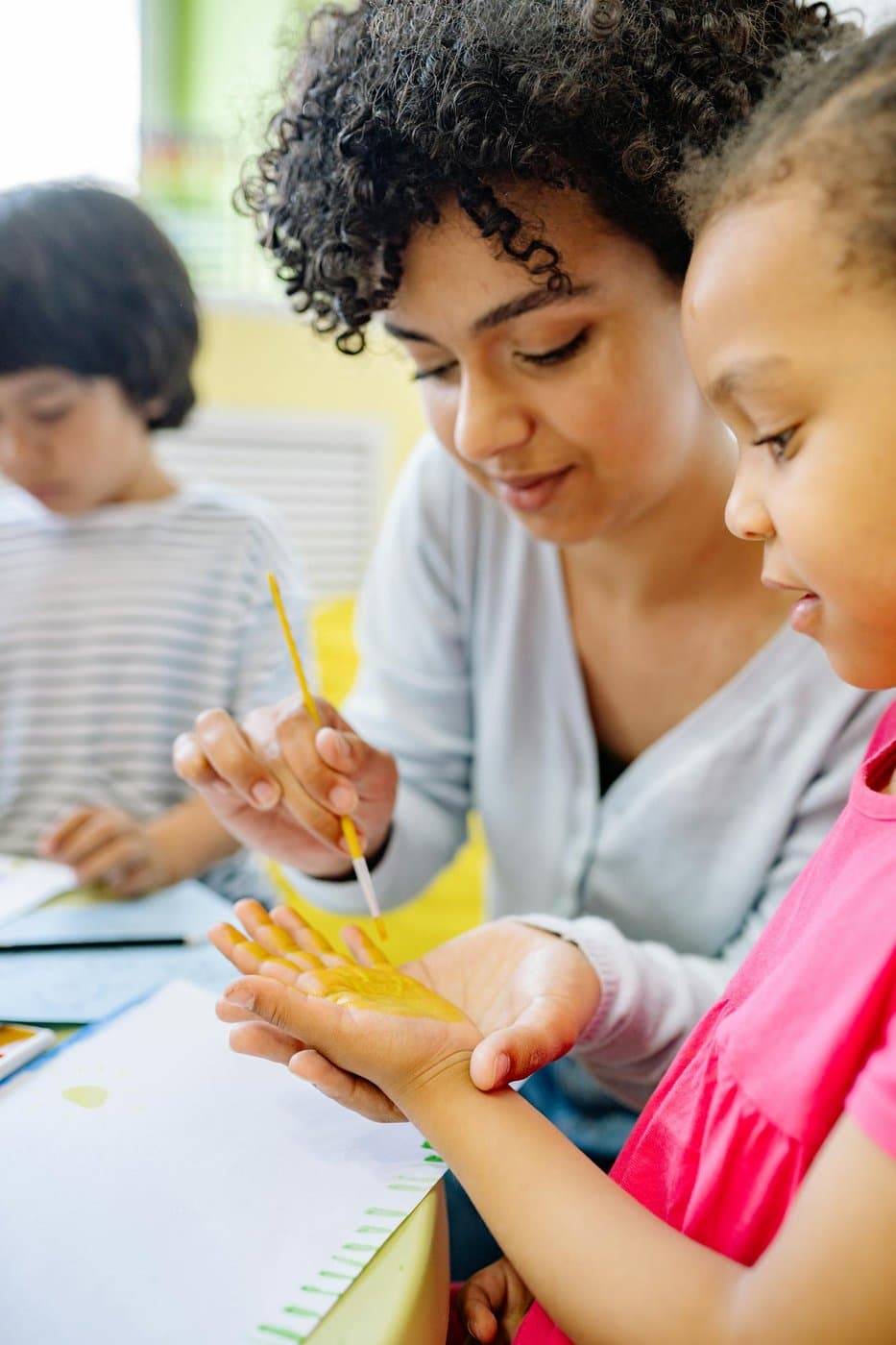 Caregiver gently helping a young girl with a creative activity