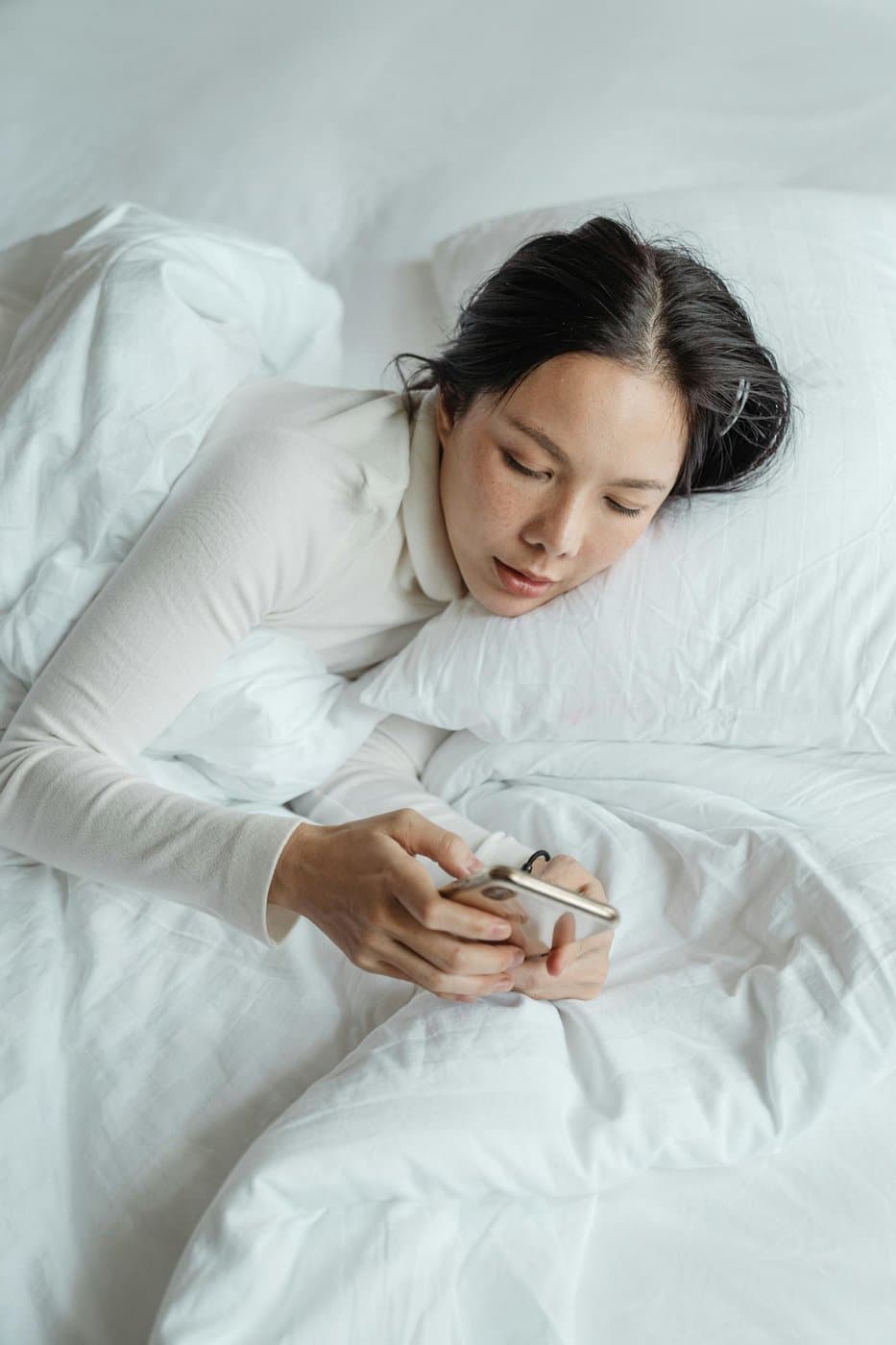 Parent resting in bed while checking her phone on a quiet morning