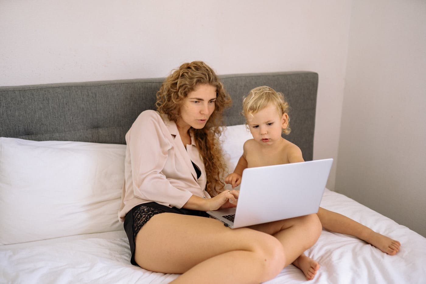 Mother and toddler sitting on the bed looking at a laptop together
