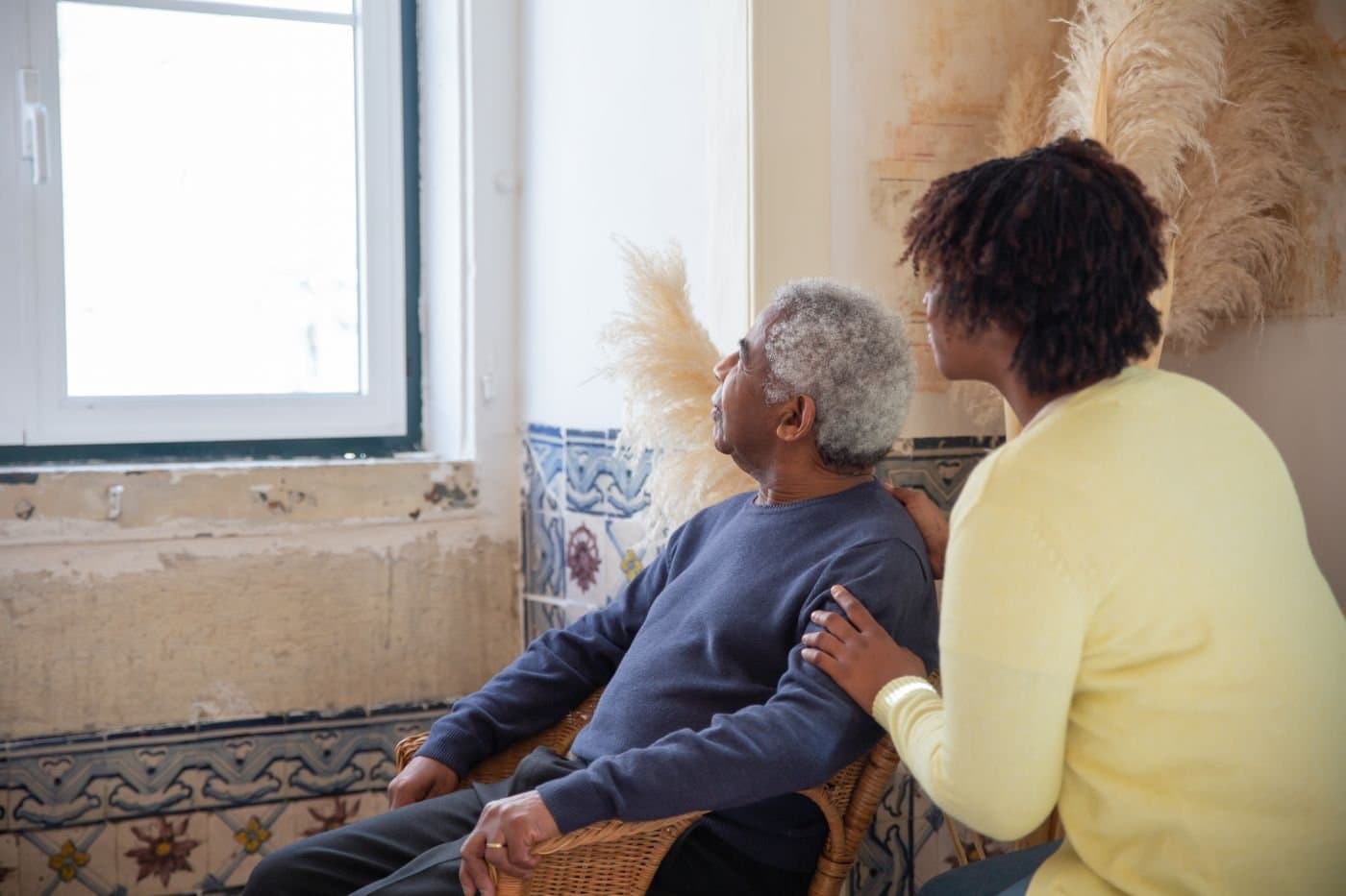 Adult daughter sitting supportively with an elderly parent by the window