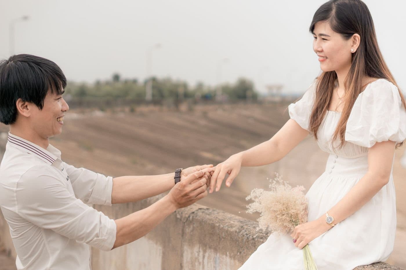 East Asian couple celebrating an engagement as he places a ring on her hand outdoors