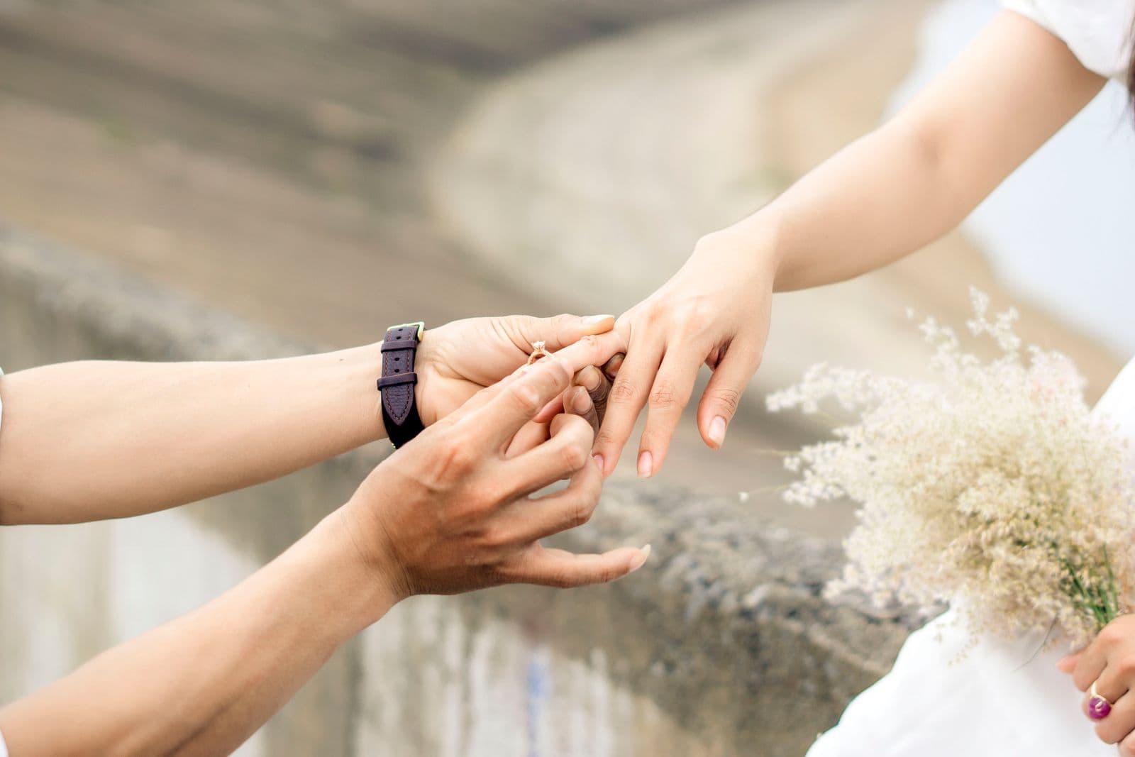 Close-up of an East Asian couple as he slides an engagement ring onto her finger outdoors