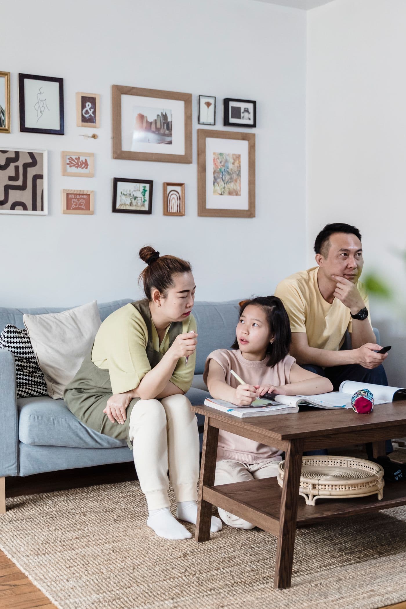 East Asian mother helping daughter with homework while father sits distracted on the sofa