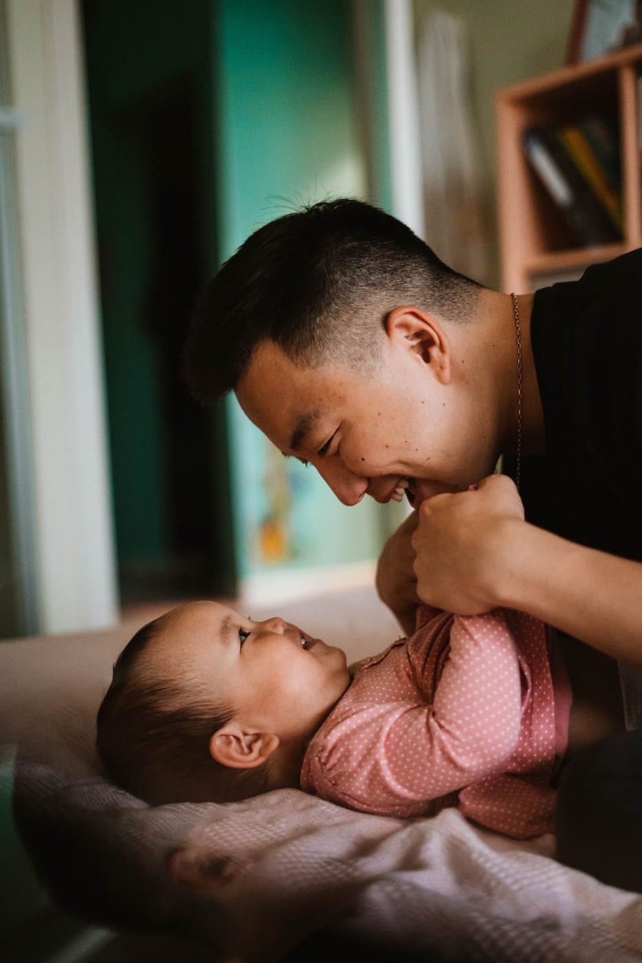 Young East Asian father playfully bonding face-to-face with his baby at home