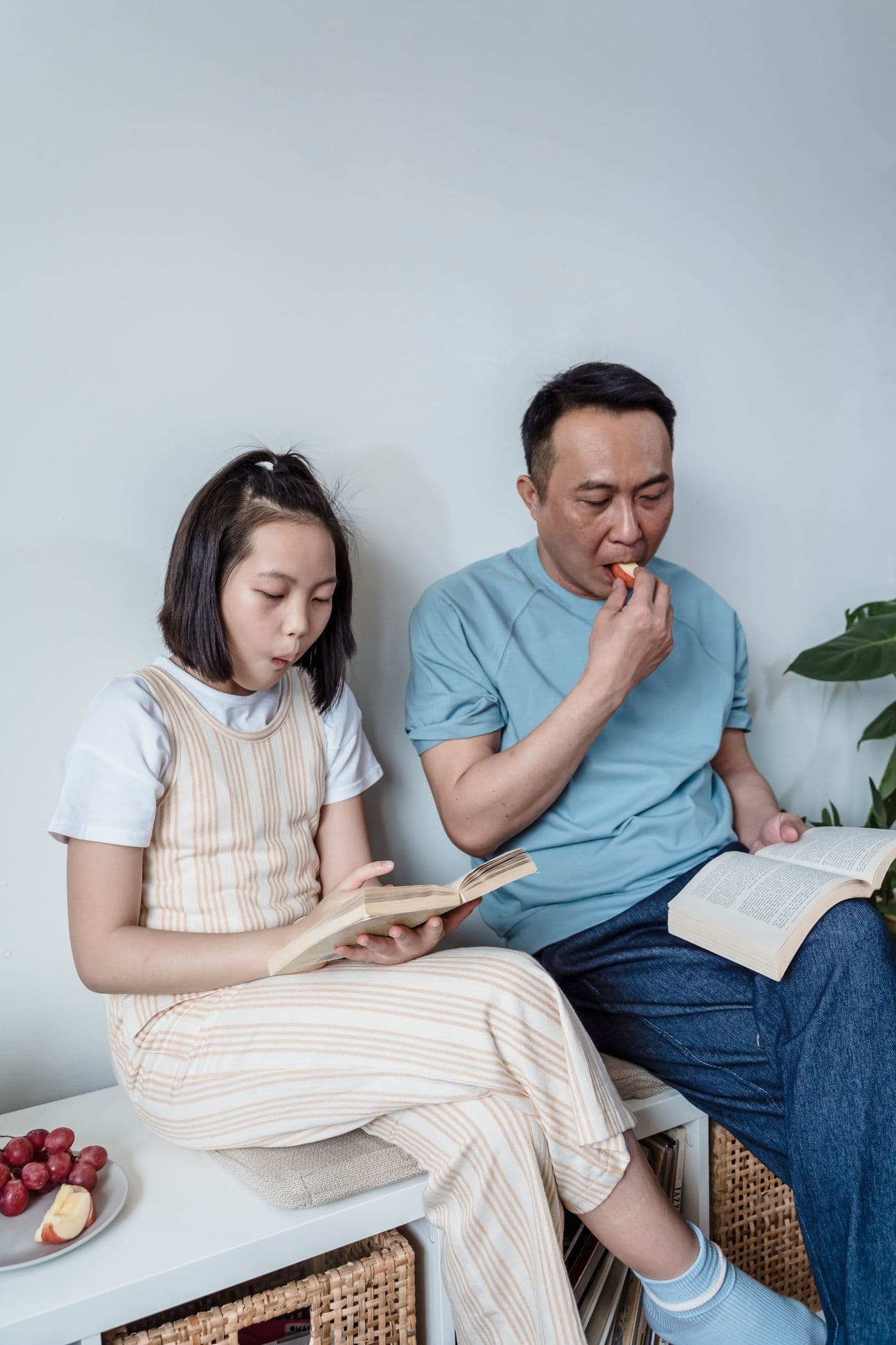 East Asian father and preteen daughter reading books together on a bench at home