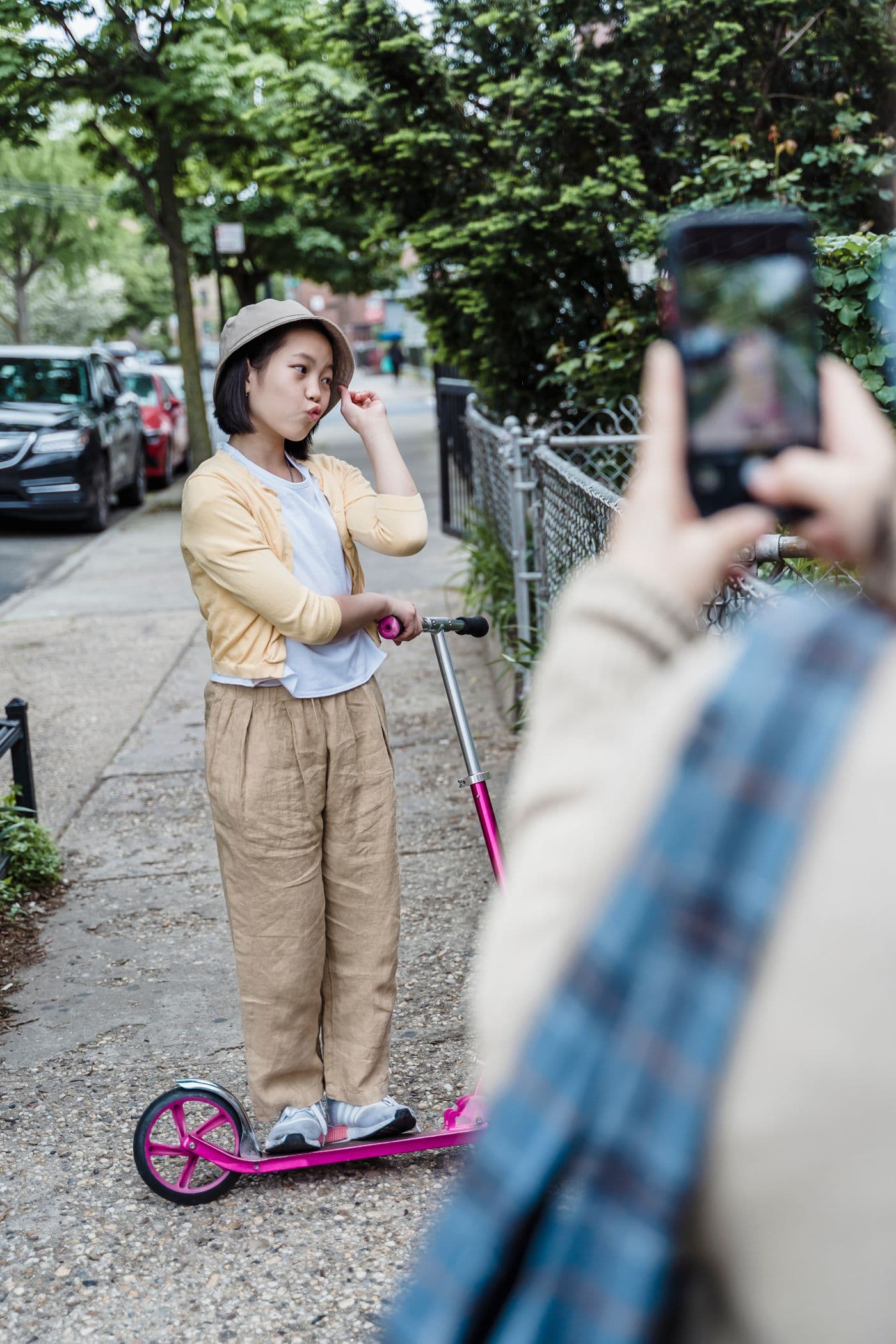 East Asian girl posing on a scooter while a family member photographs her outdoors