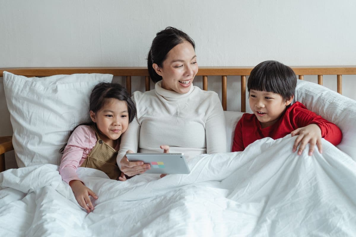 East Asian mother and children gathered on the bed looking at a tablet together
