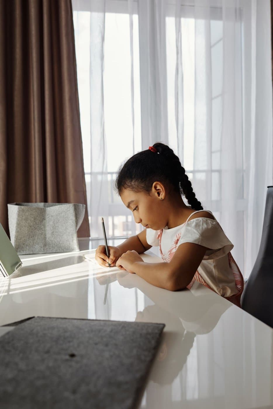 Child focused on writing and schoolwork at a desk by the window