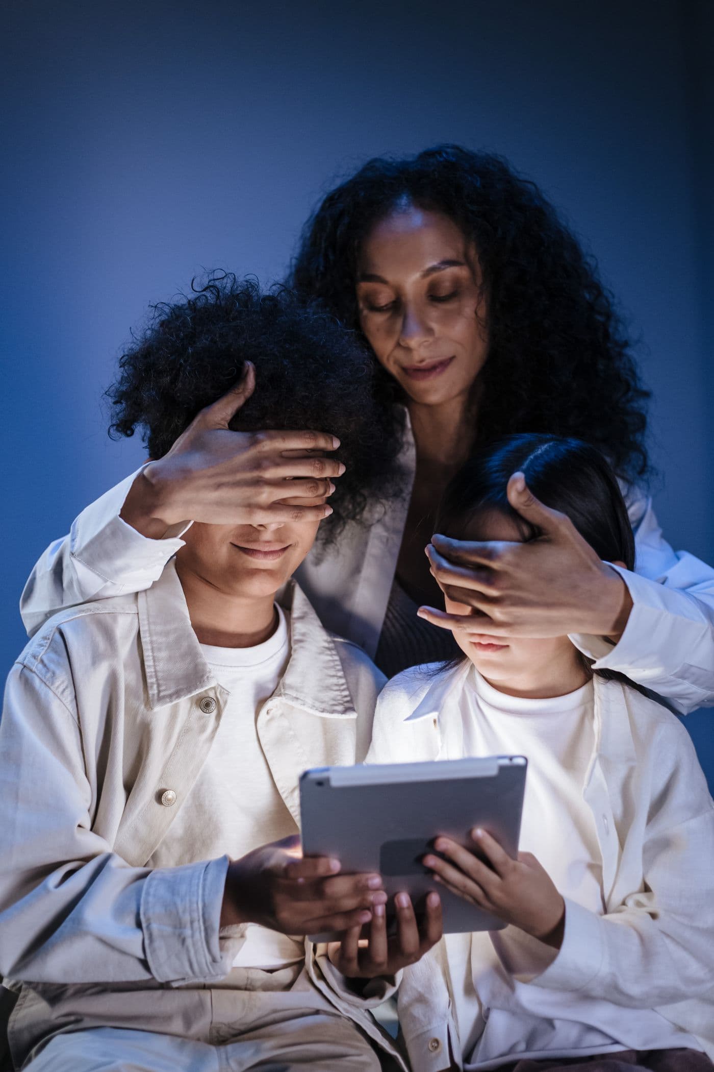 Mother gently covering her children's eyes while blocking inappropriate internet content on a tablet