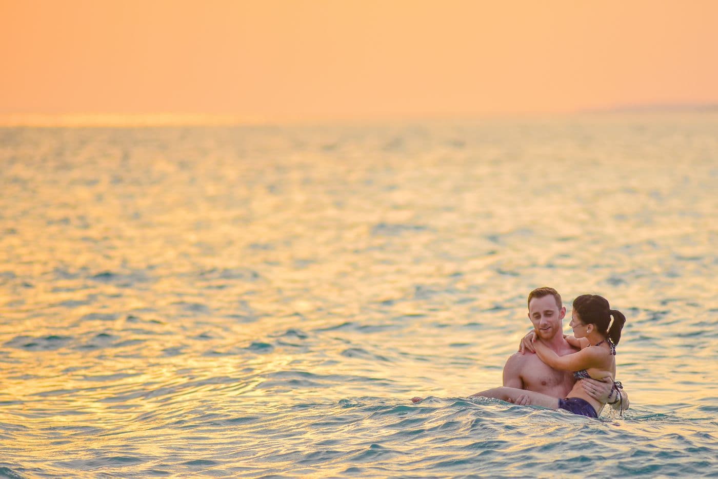 Couple holding each other in the ocean during a quiet golden-hour moment