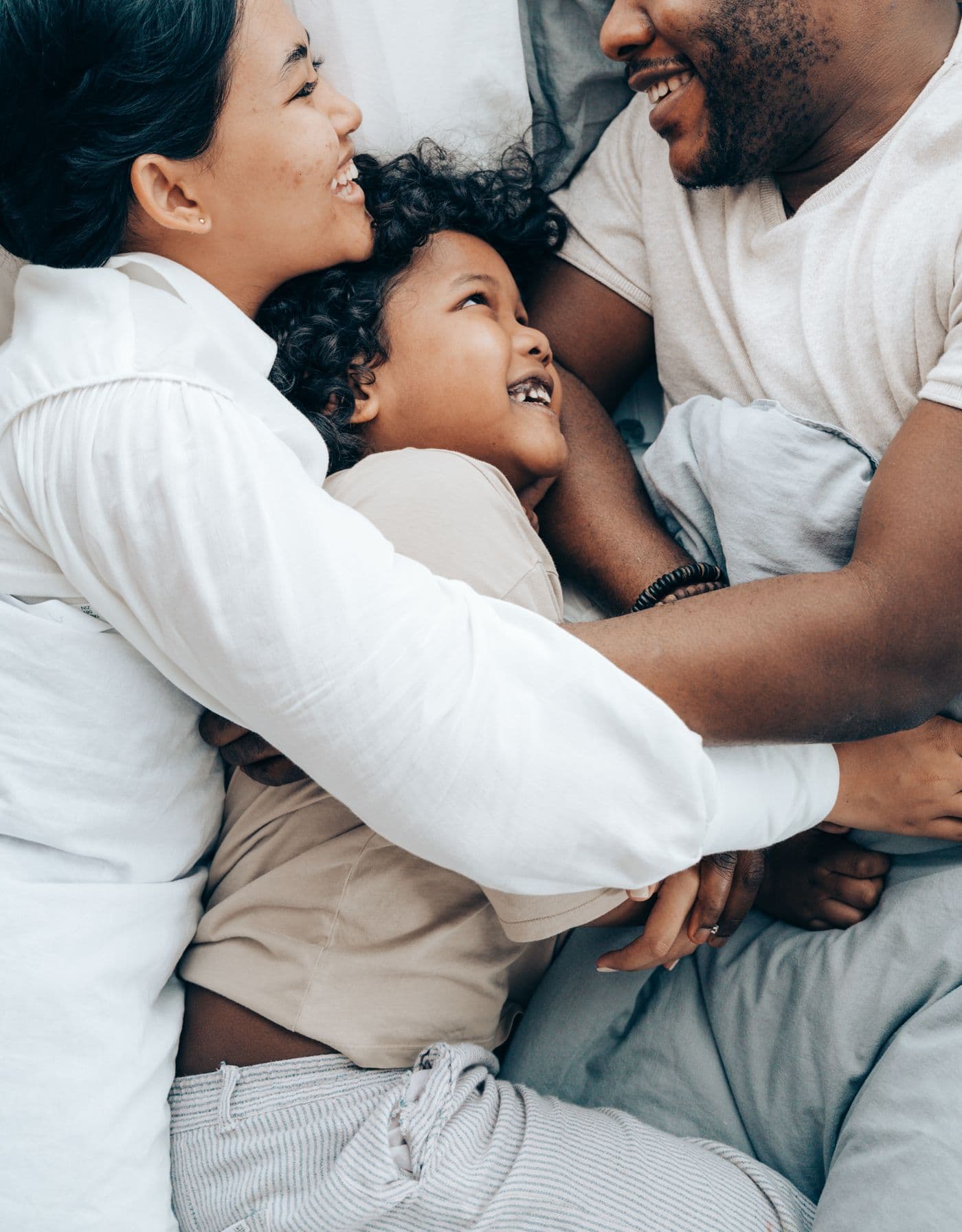 Multicultural parents cuddling with their young child on the bed at home
