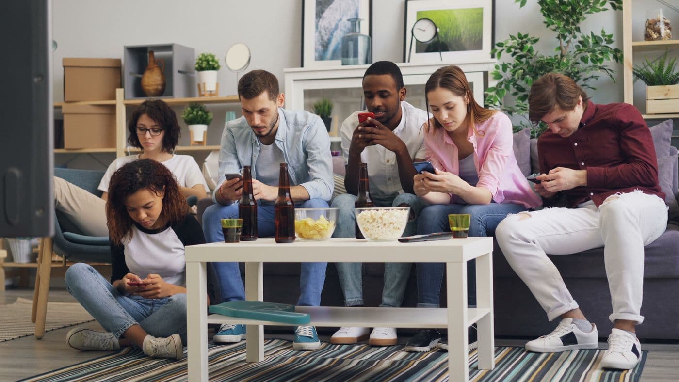Diverse group of adults sitting together on a couch, each focused on their own smartphone