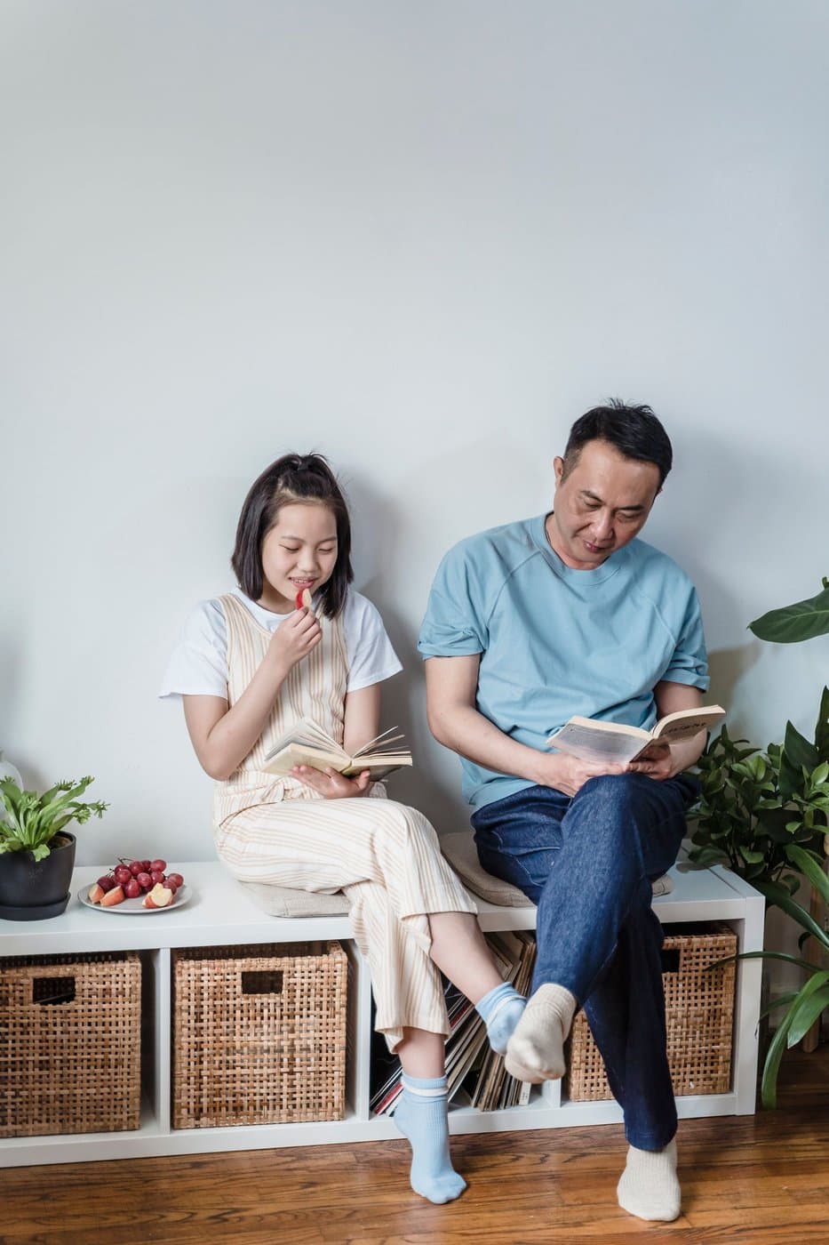 East Asian father and daughter reading together at home on a storage bench