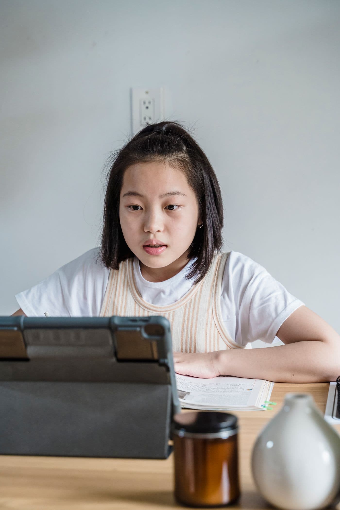 East Asian girl focused on a tablet at a desk, practicing language or schoolwork at home