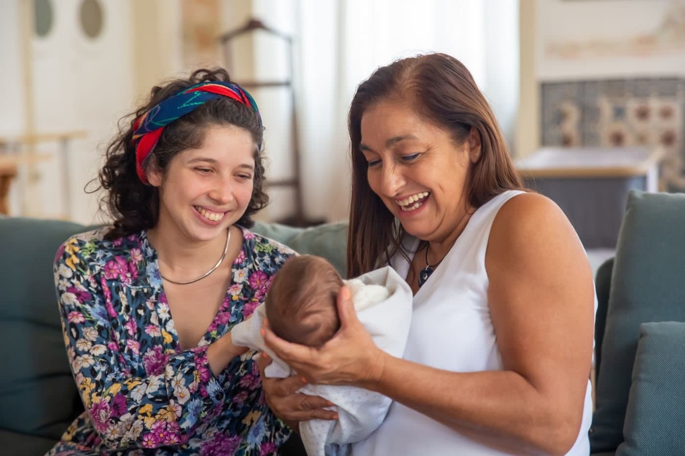 Grandmother smiling while holding a newborn with the baby's mother nearby