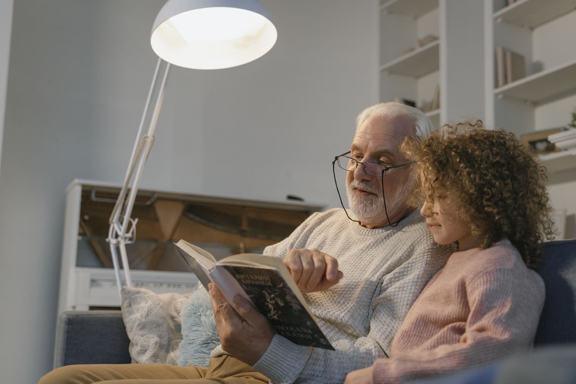 A grandfather and a child reading a book together on a sofa