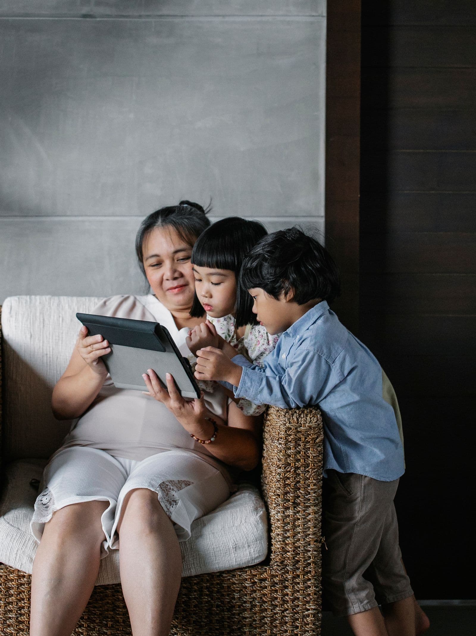 East Asian grandmother and two grandchildren gathered around a tablet at home