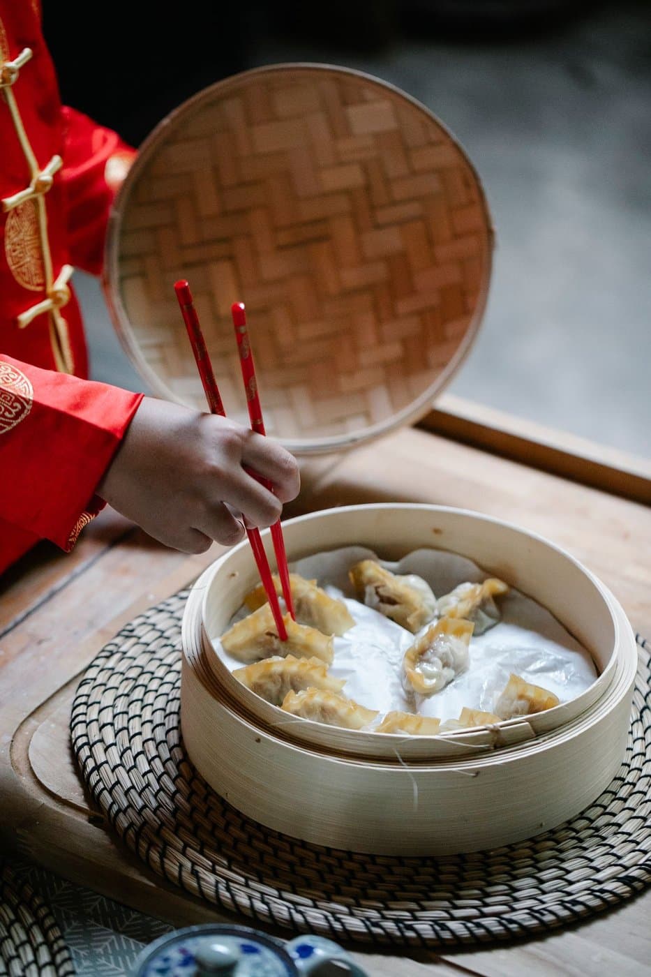 Child serving dumplings from a bamboo steamer during a family meal