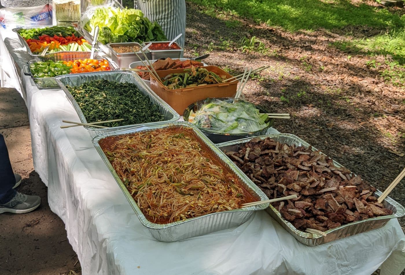 Korean potluck spread with grilled meat, kimchi, namul, and fresh vegetables for wrapping