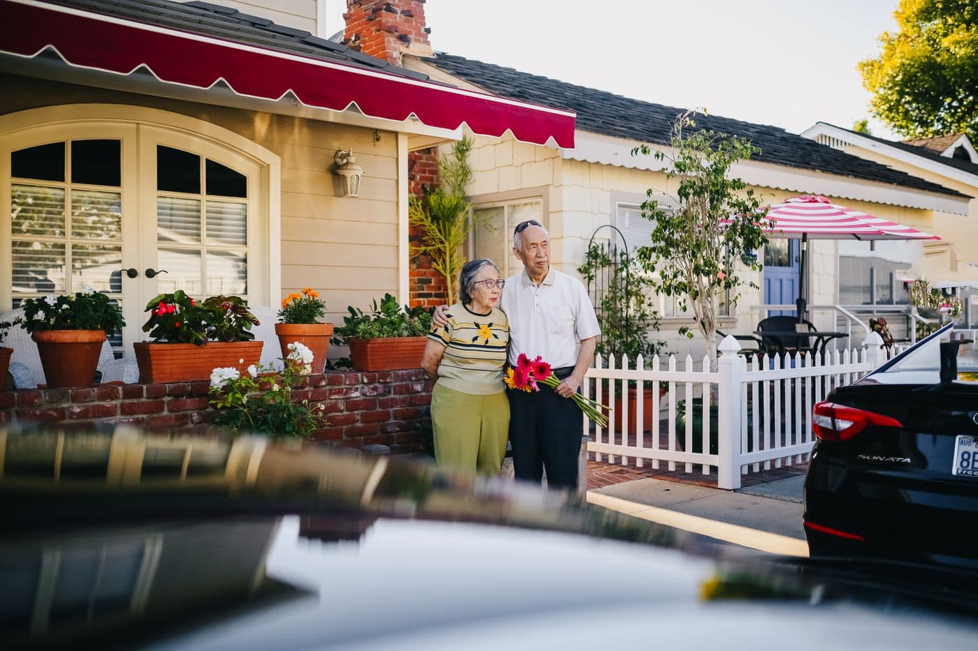 East Asian grandparents standing together outside their home, ready for a family visit