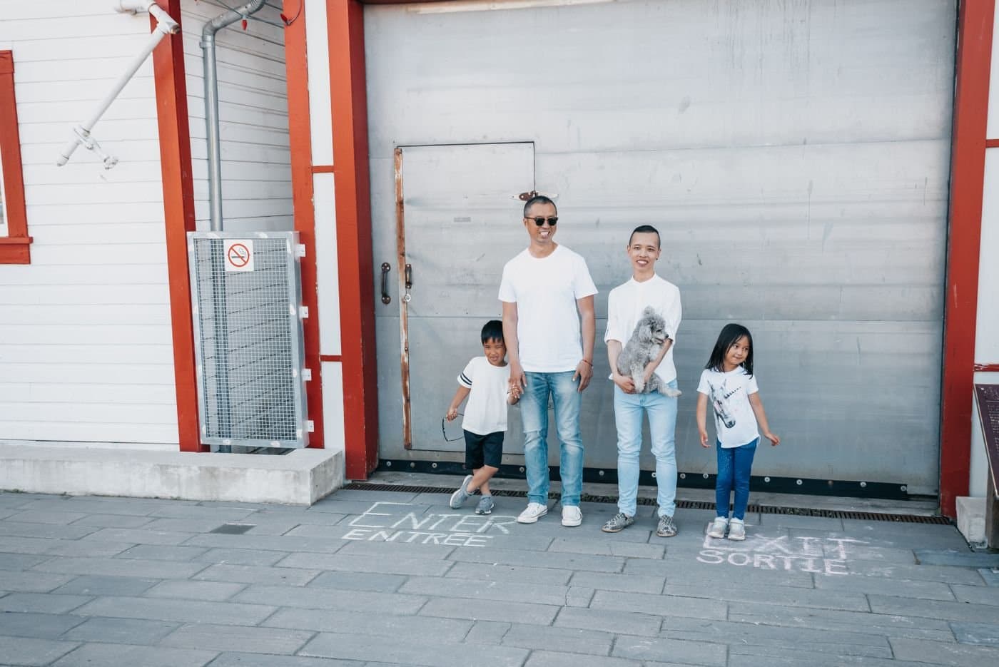 Family of four walking together along a sunny city sidewalk