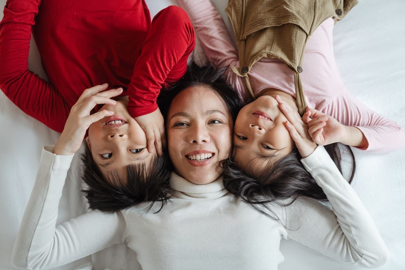 Mother and children lying together on a white bed, smiling at the camera