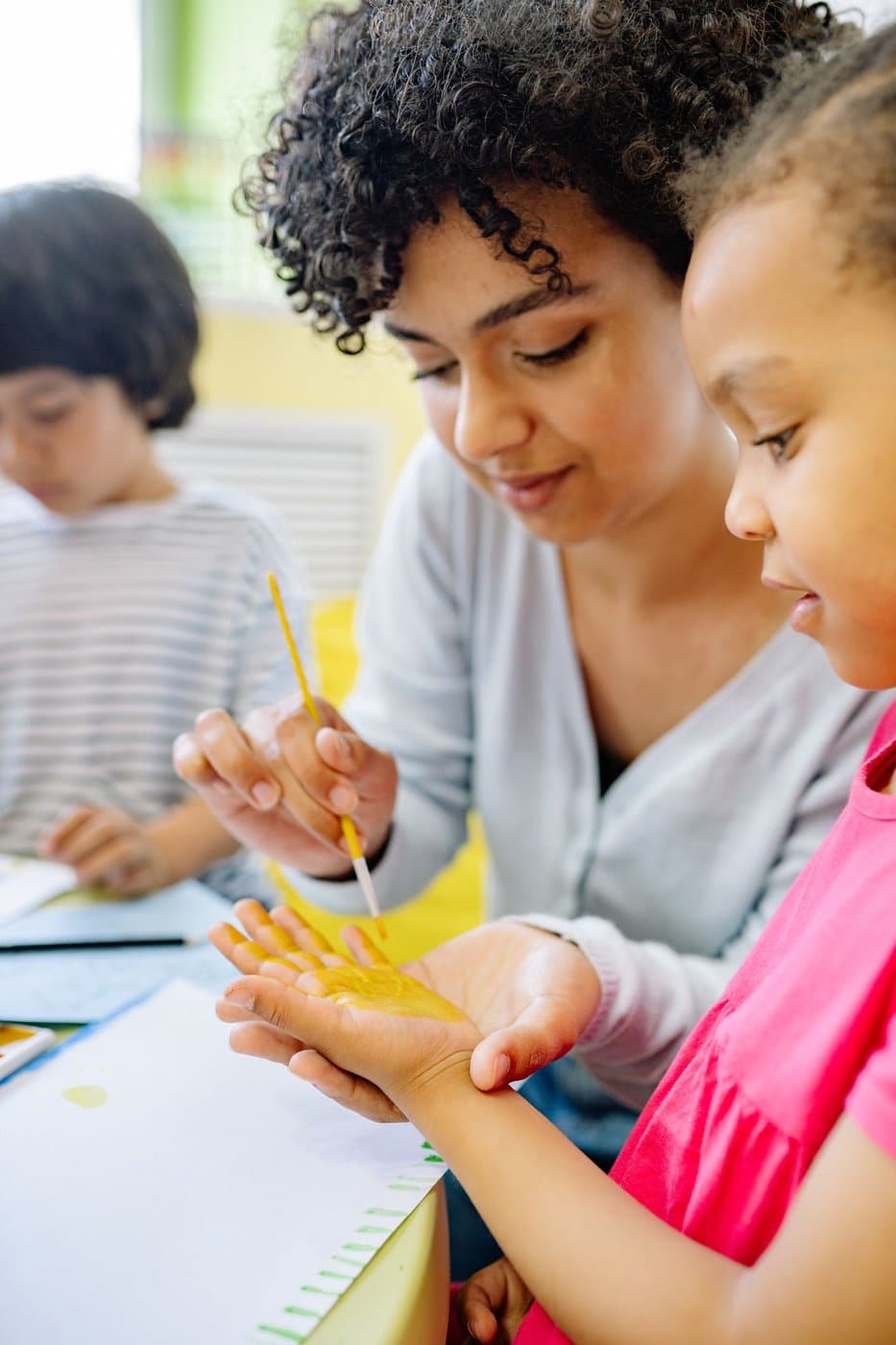 Caregiver gently helping a young girl with a creative activity