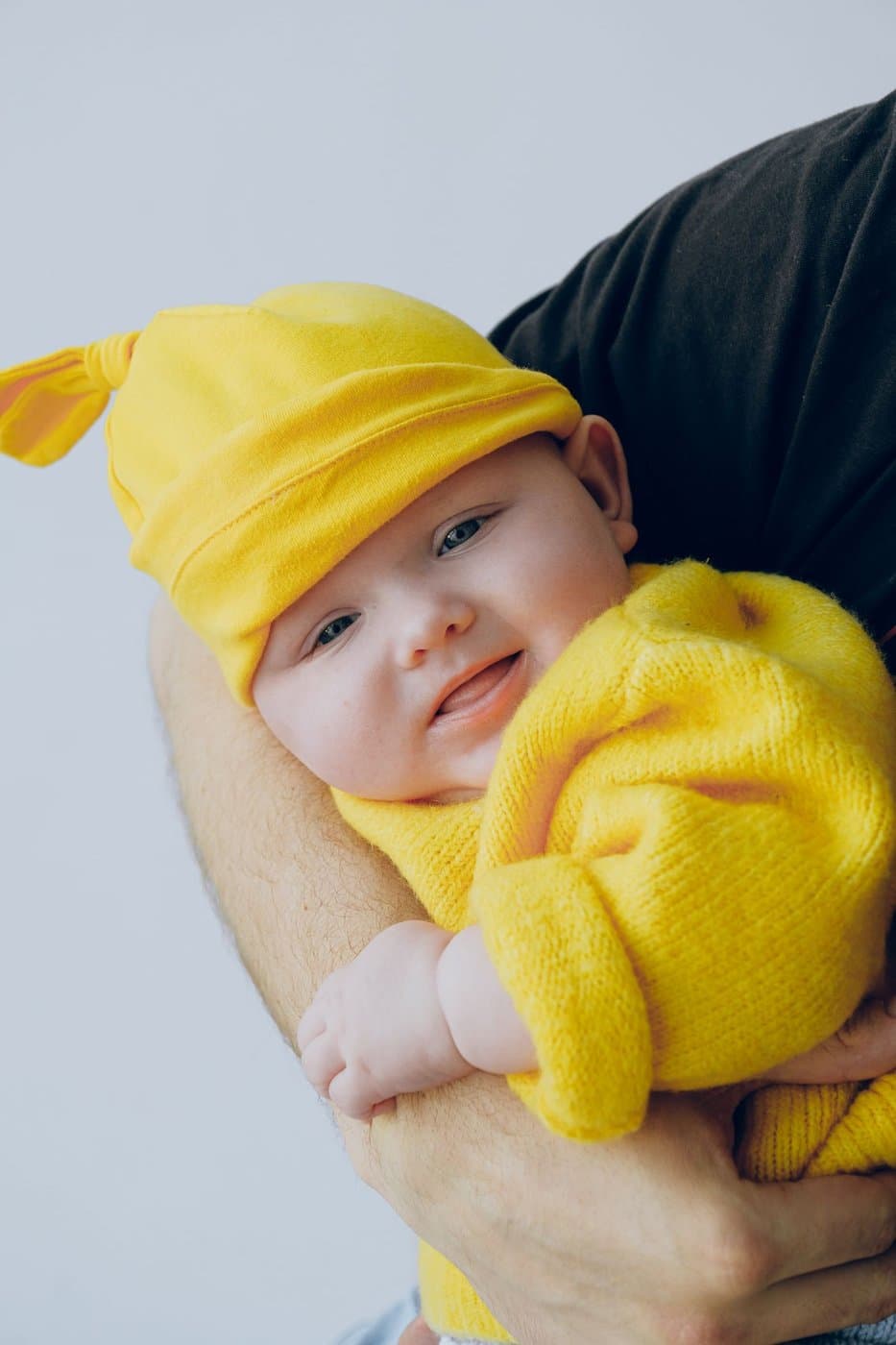 Smiling baby in a yellow knit outfit held close by a parent