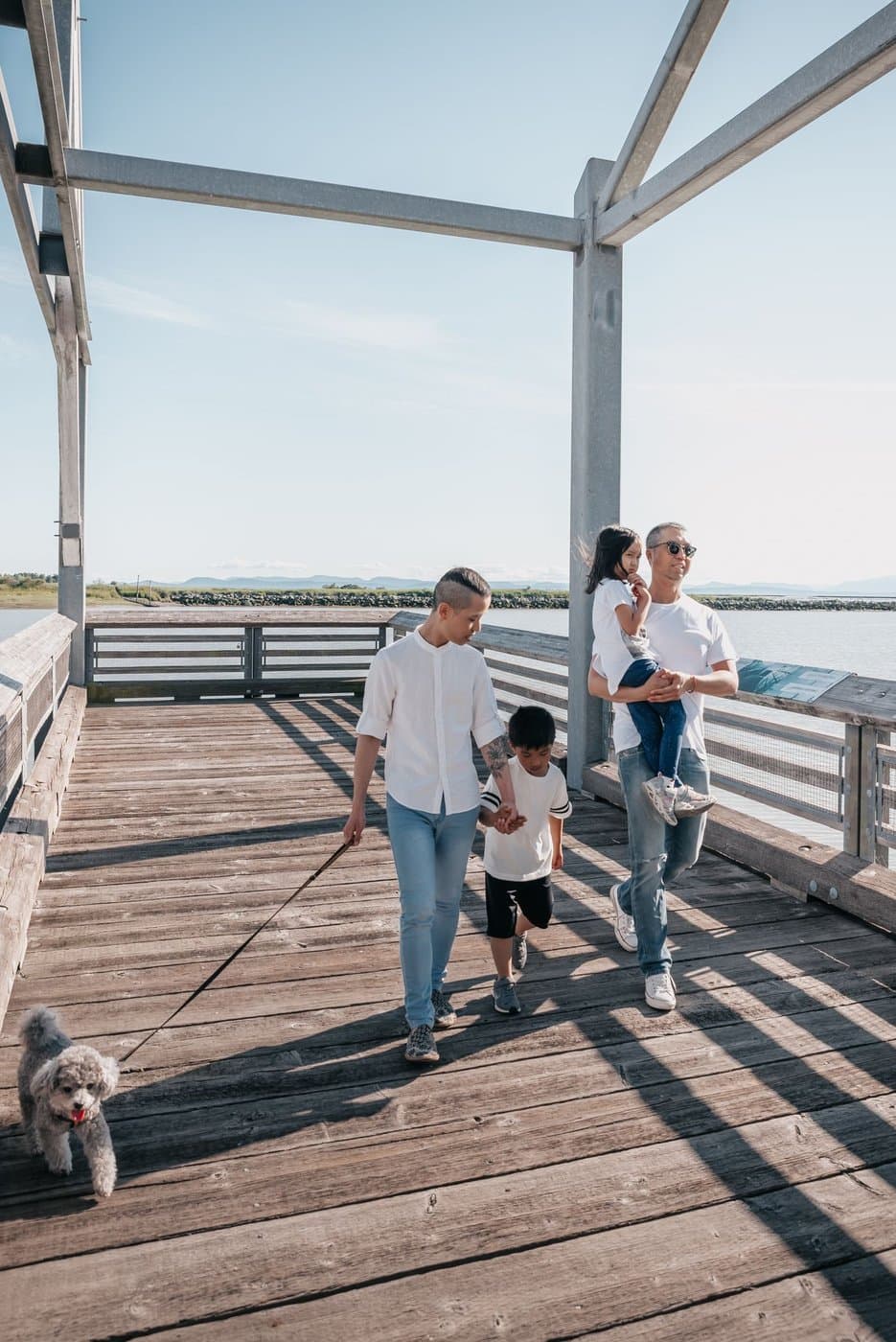 Parents walking outdoors with young children along a sunny boardwalk