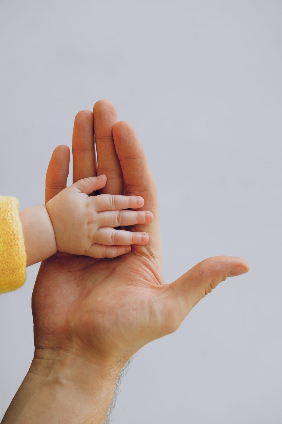 New parent's hand gently cradling a baby's tiny hand