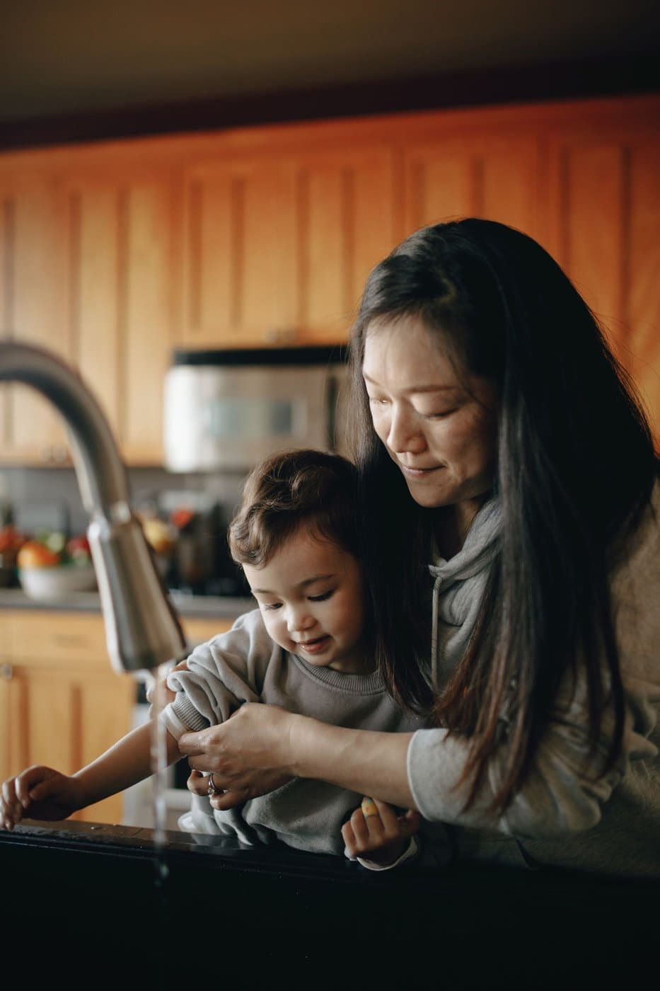 Mother helping her toddler roll up sleeves before washing hands at the sink