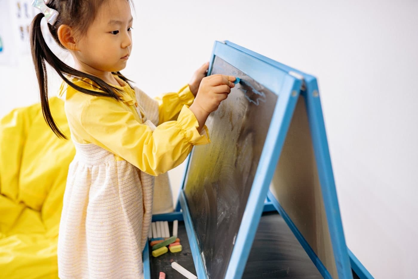 Young child drawing at a chalkboard easel with an adult nearby