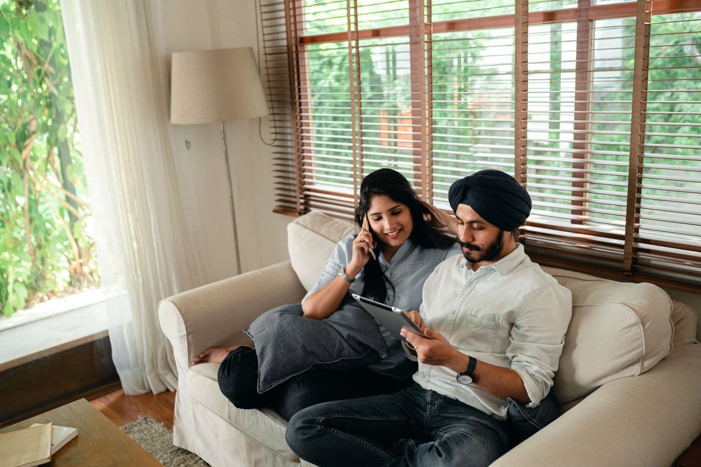 Indian father relaxing at home on the couch while his partner uses a phone nearby