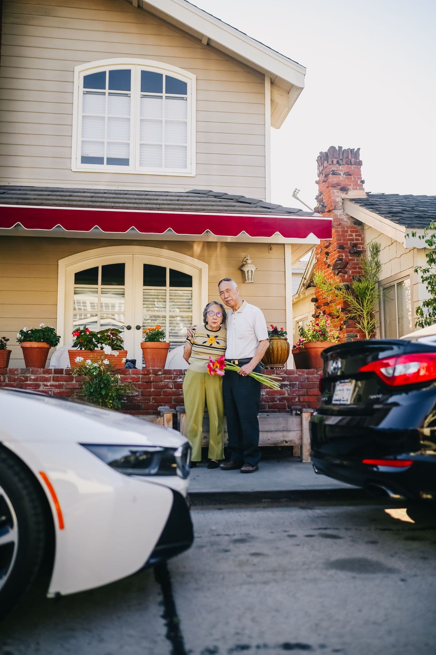 East Asian grandparents standing together outside their suburban home