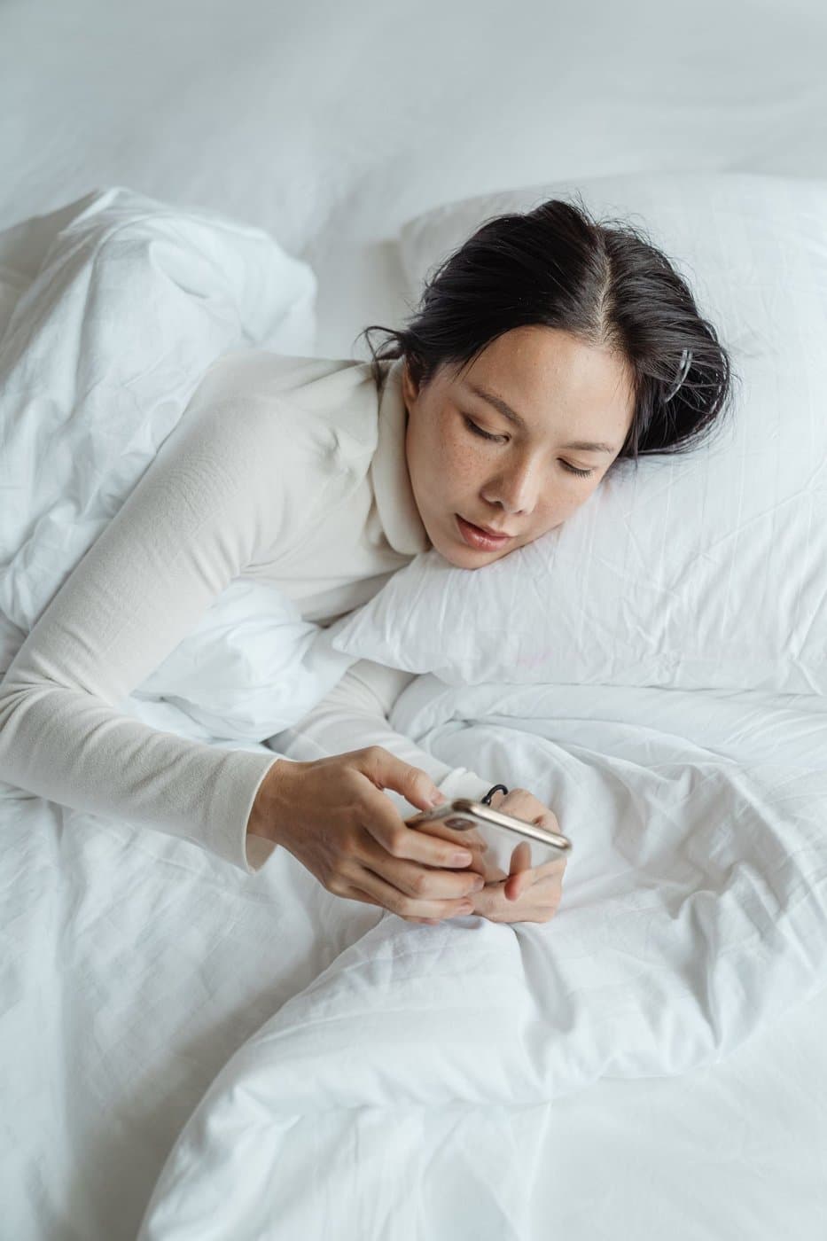 Parent resting in bed while checking her phone on a quiet morning