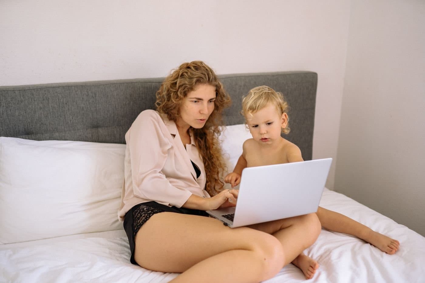 Mother and toddler sitting on the bed looking at a laptop together