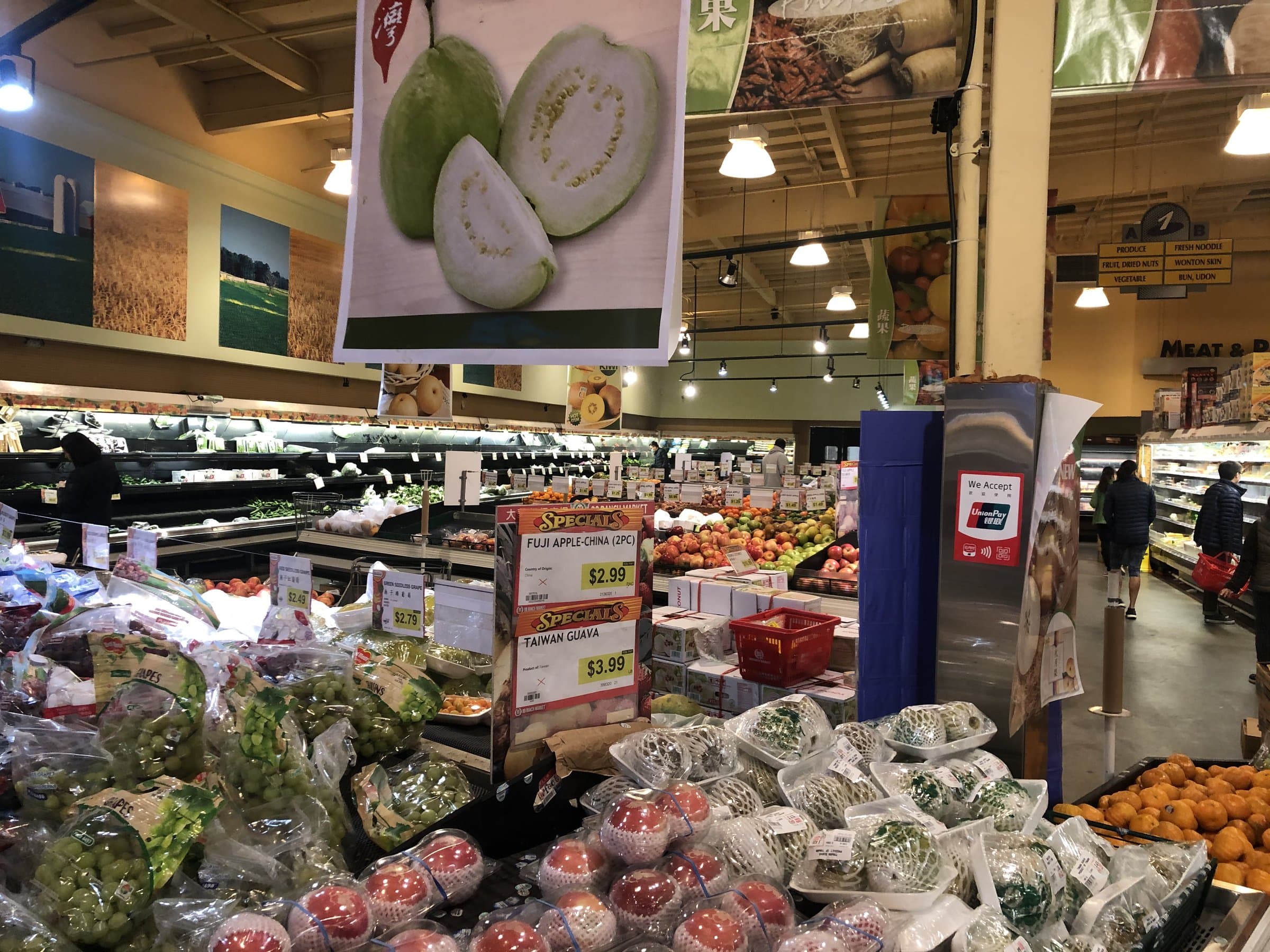 Produce aisle at a 99 Ranch Market with Taiwan guava and Fuji apple specials under bright overhead lights