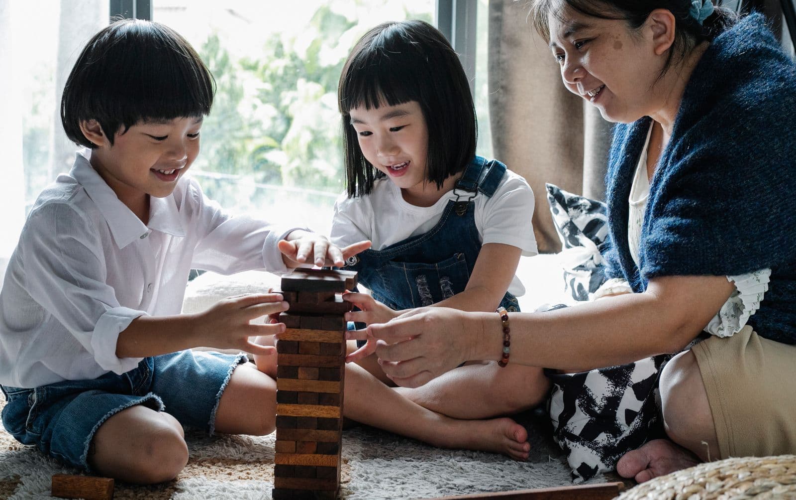 East Asian grandmother helping two young children build a wooden block tower at home