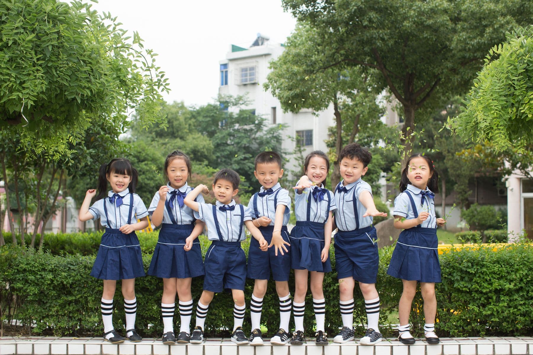 Group of East Asian elementary schoolchildren standing together on a landscaped school campus