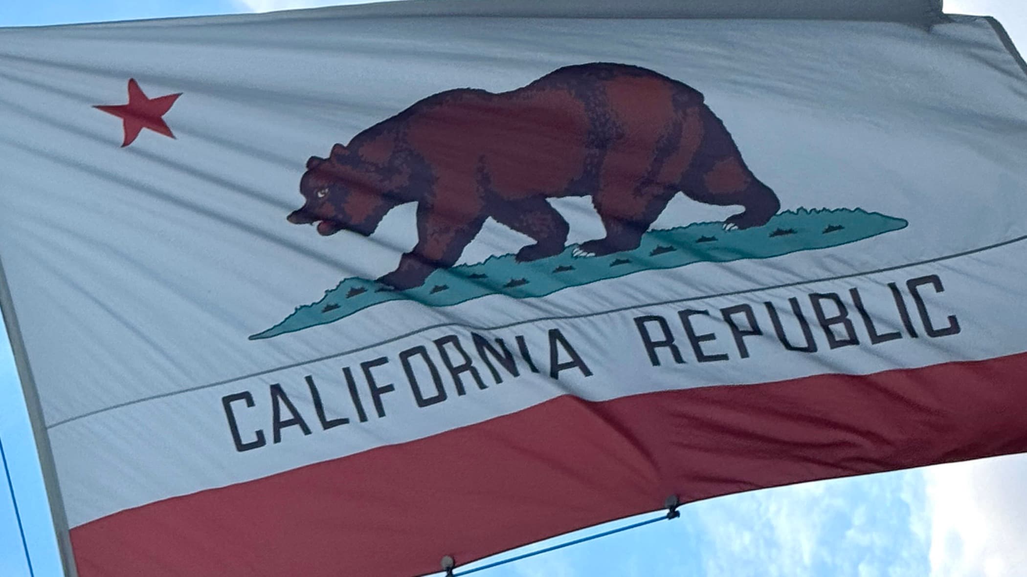 California state flag flying against a blue sky, with the grizzly bear and the words California Republic