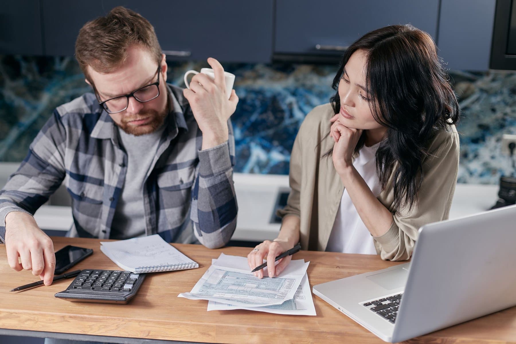 Couple reviewing bills with a calculator and laptop at their kitchen table