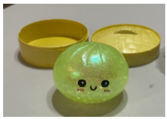Translucent squishy bun toy filled with water beads and glitter beside a yellow steamer-style plastic case