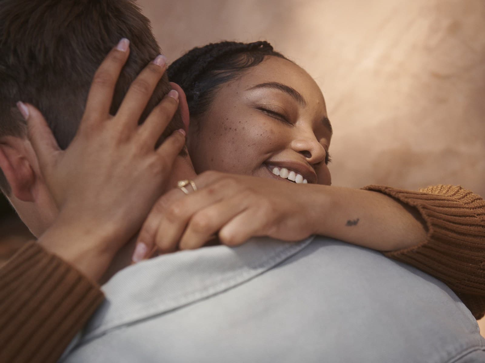 Couple in a warm outdoor embrace, one partner smiling with eyes closed