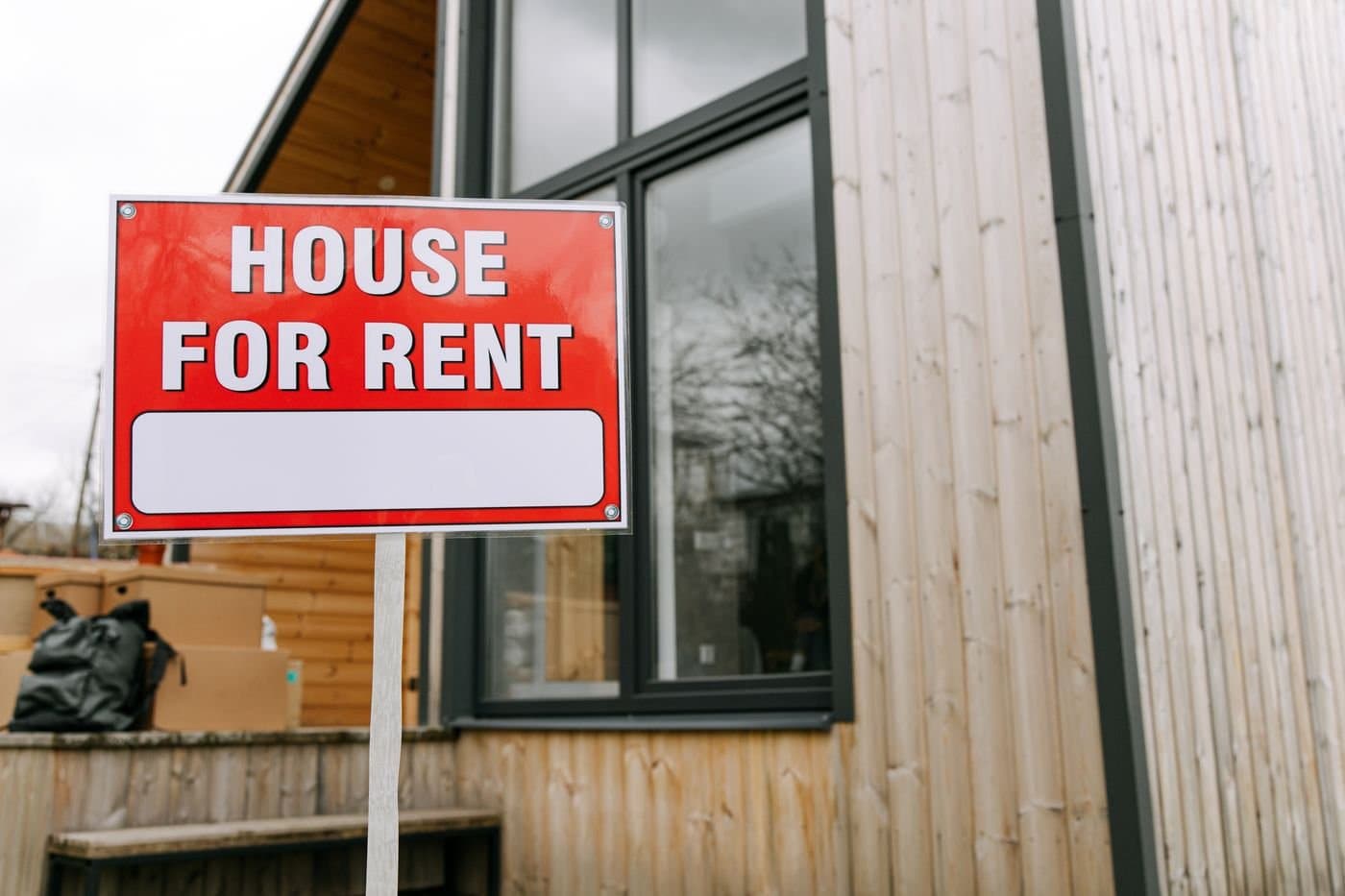 Red House for Rent sign planted in front of a modern wooden home