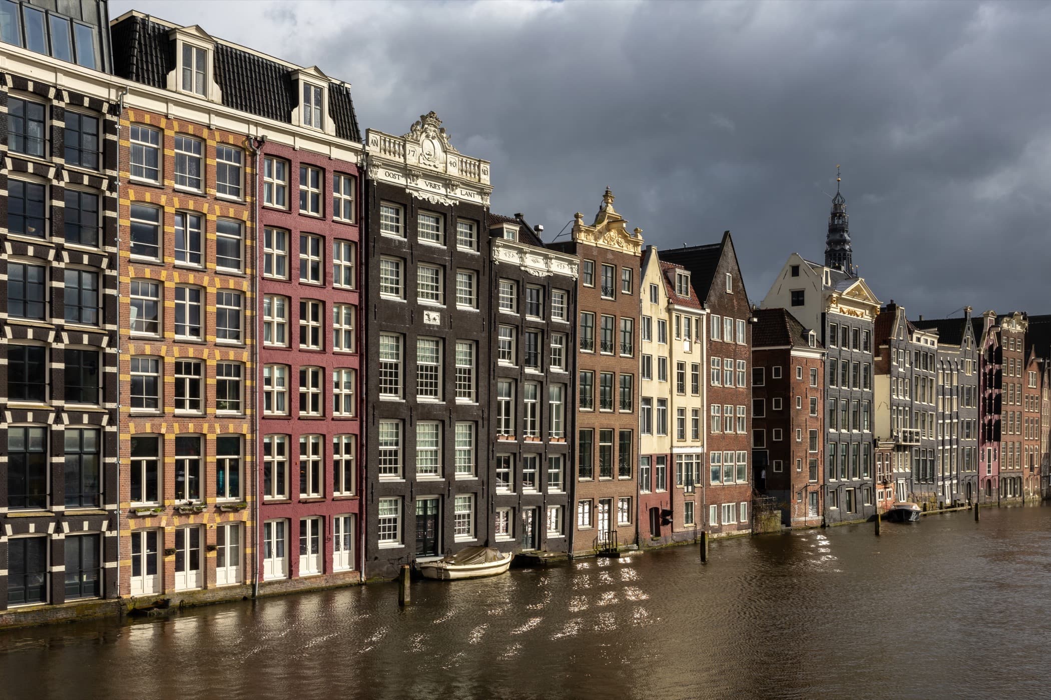 Row of Amsterdam canal houses along Damrak under dramatic clouds, with no people in frame