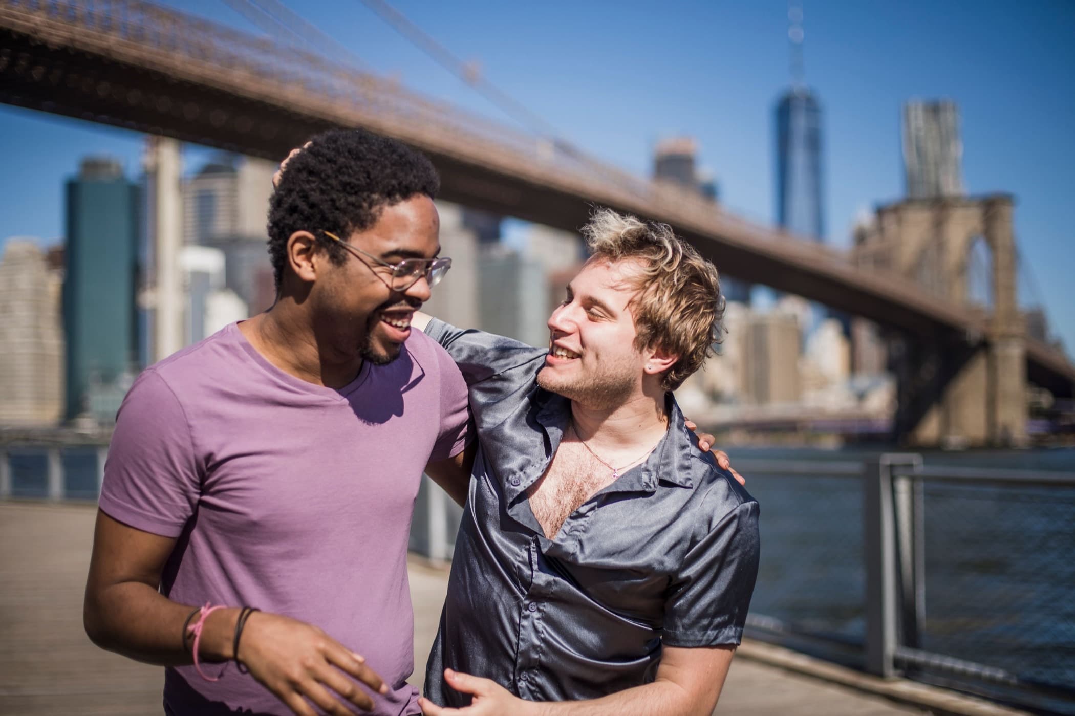 Interracial couple smiling outdoors with the Brooklyn Bridge behind them