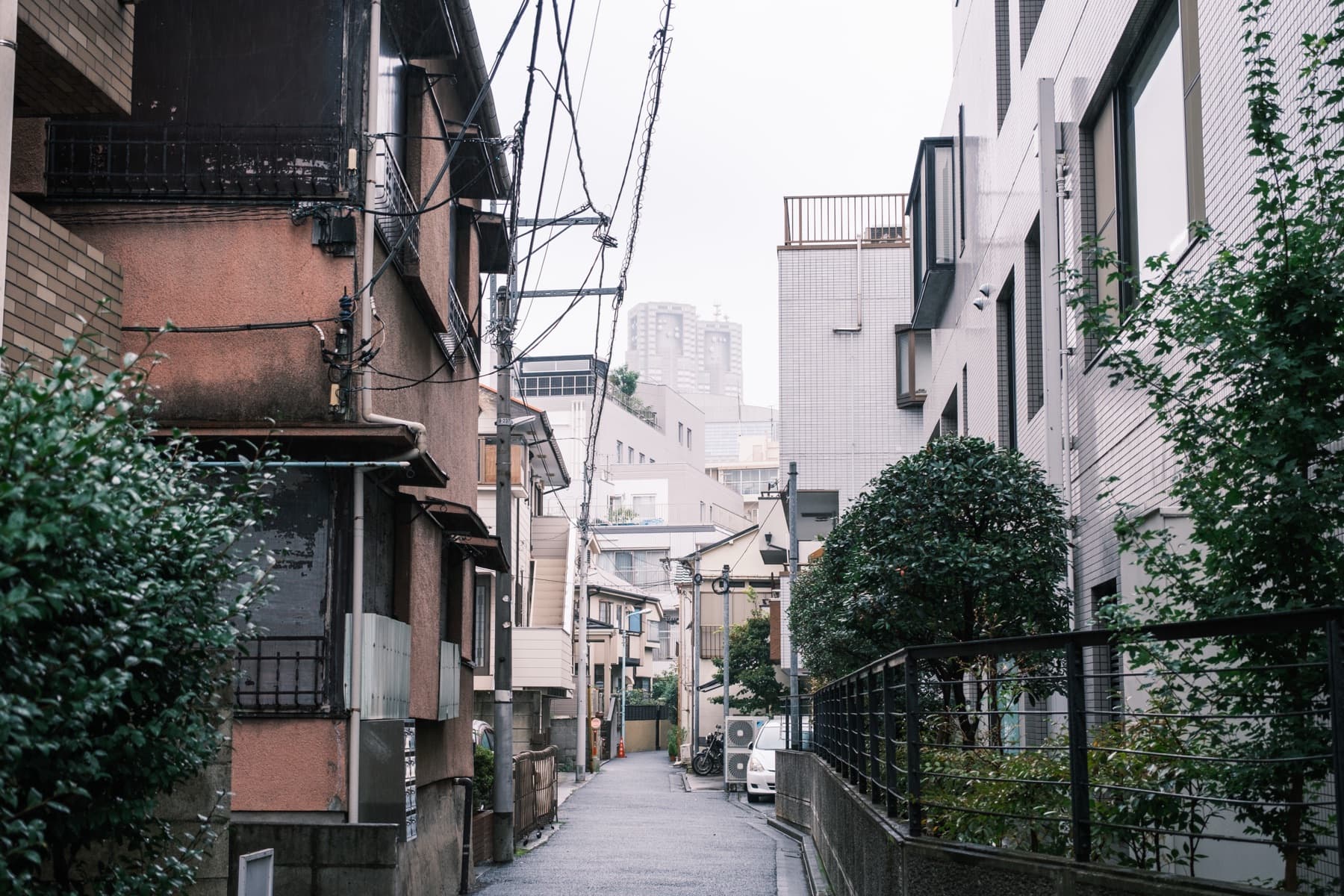 A narrow residential lane in Shinjuku, Tokyo, lined with apartment balconies and overhead wires
