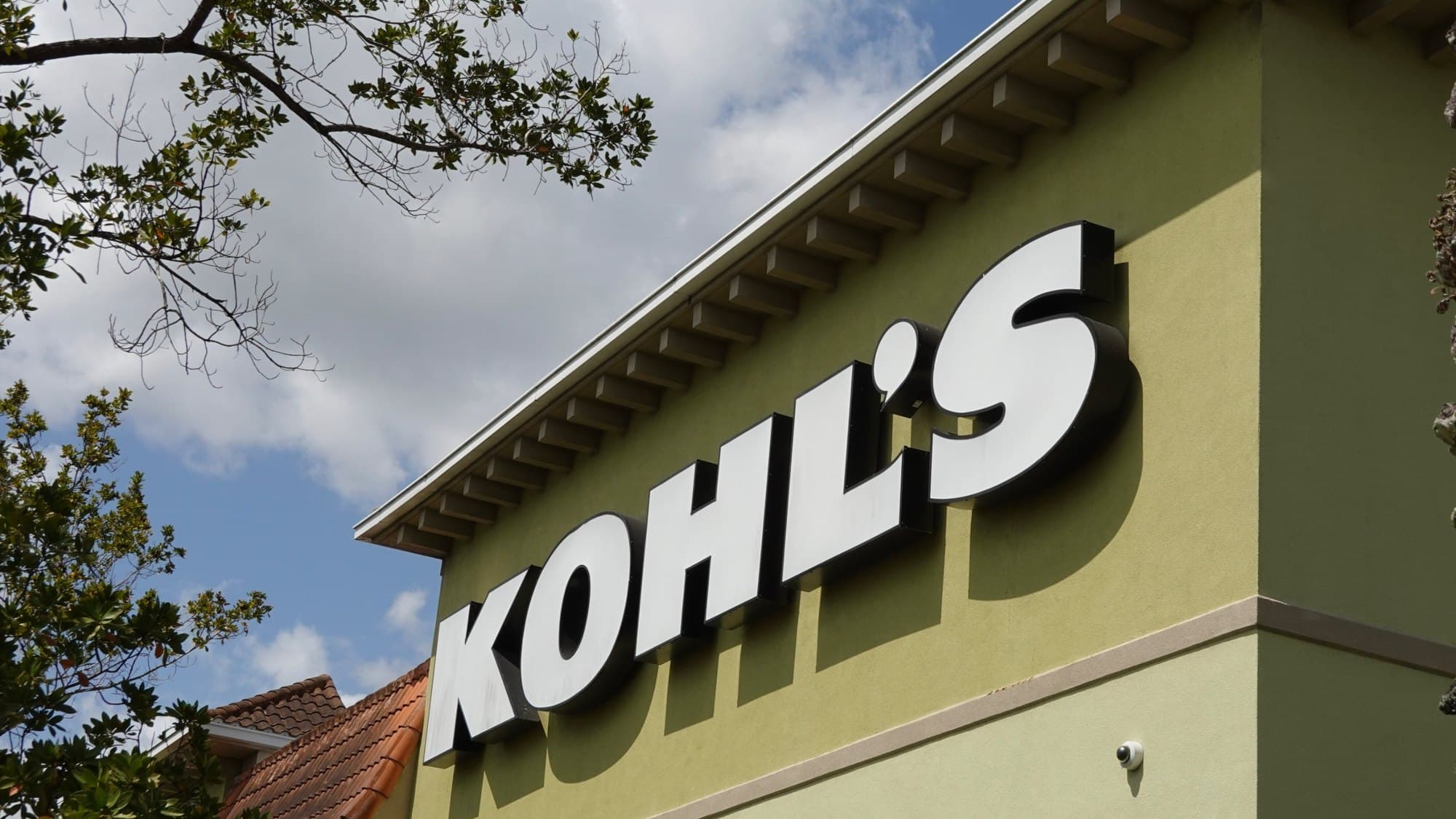 White KOHL’S storefront letters on a green building wall under blue sky