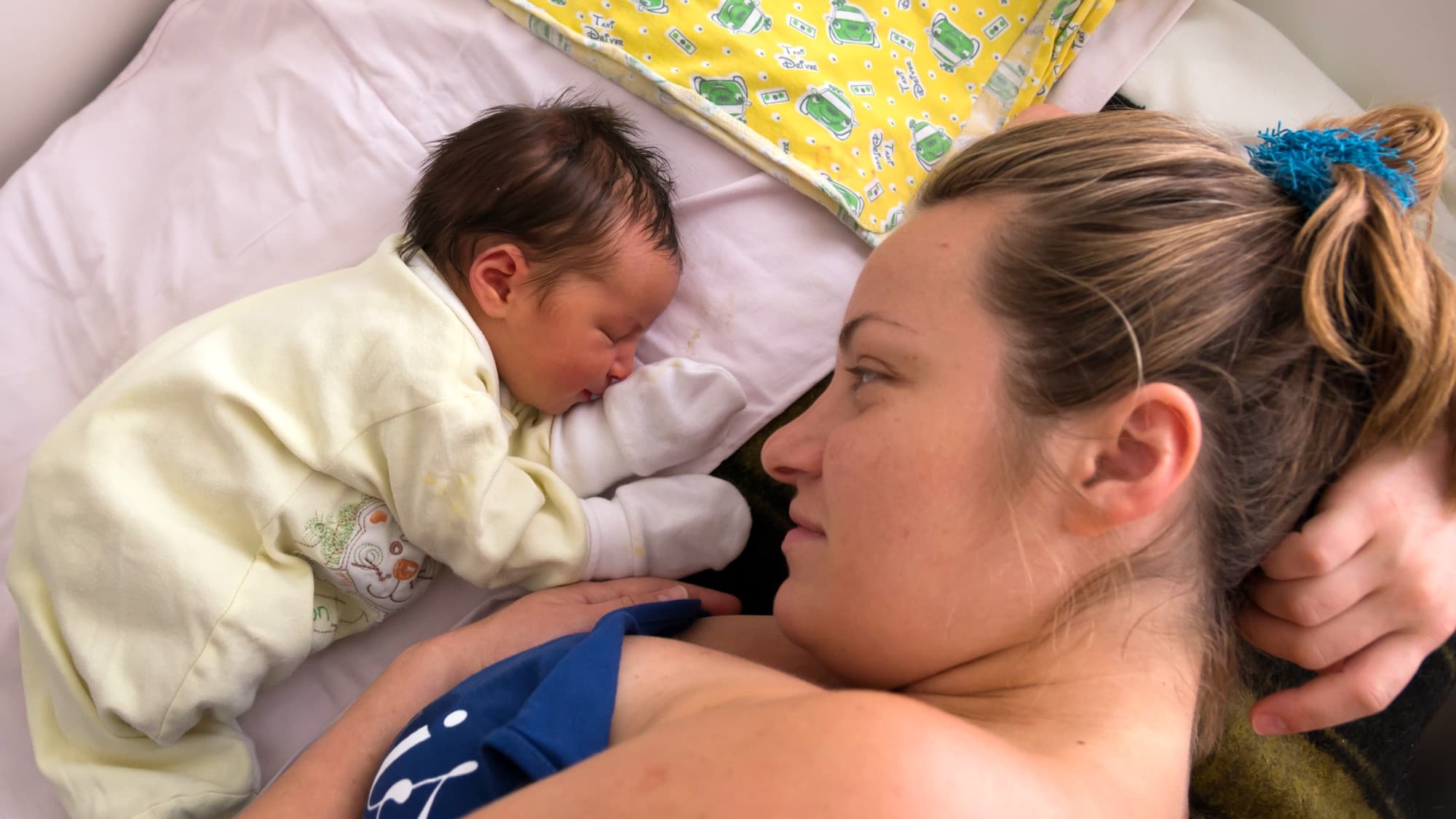 A mother lying beside her sleeping three-day-old on a pale sheet